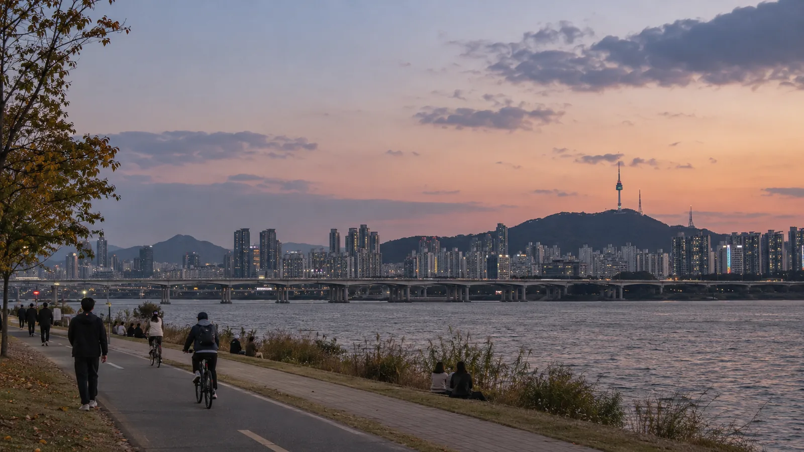 Walkers and cyclists on a Han River path at sunset, with N Seoul Tower on Namsan across the river