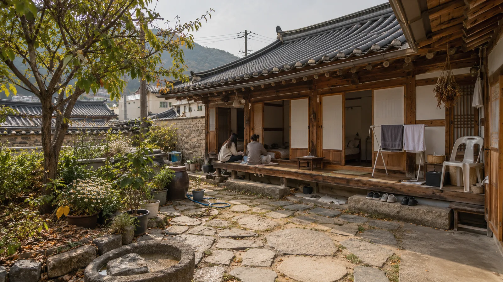 Guests sitting on the wooden porch of a hanok guesthouse courtyard with a laundry rack and shoes by the step